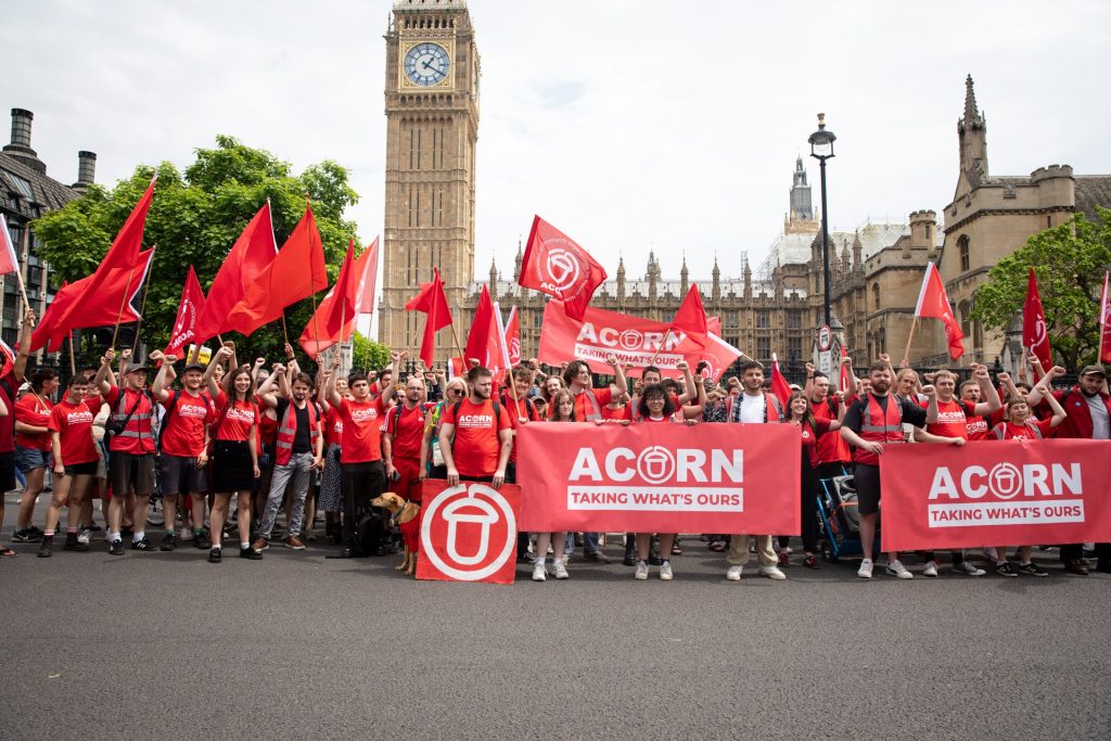 A lot of Acorn members, with banners and red flags, in front of the Houses of Parliament.